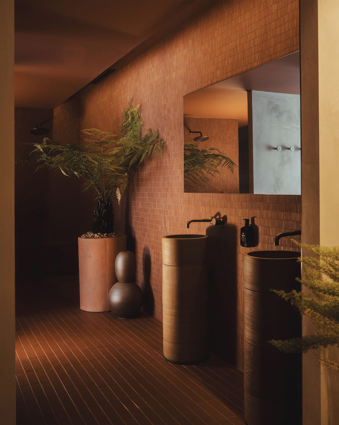The bathroom at Capybara bathhouse, featuring Leif Hand Wash, stone basins, red tiles and a large fern
