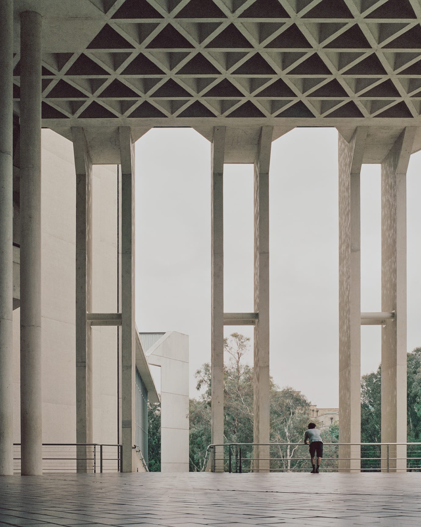 The outdoor foyer at the National Gallery of Australia, featuring graphic concrete elements, tiled flooring and gumtrees in the background.