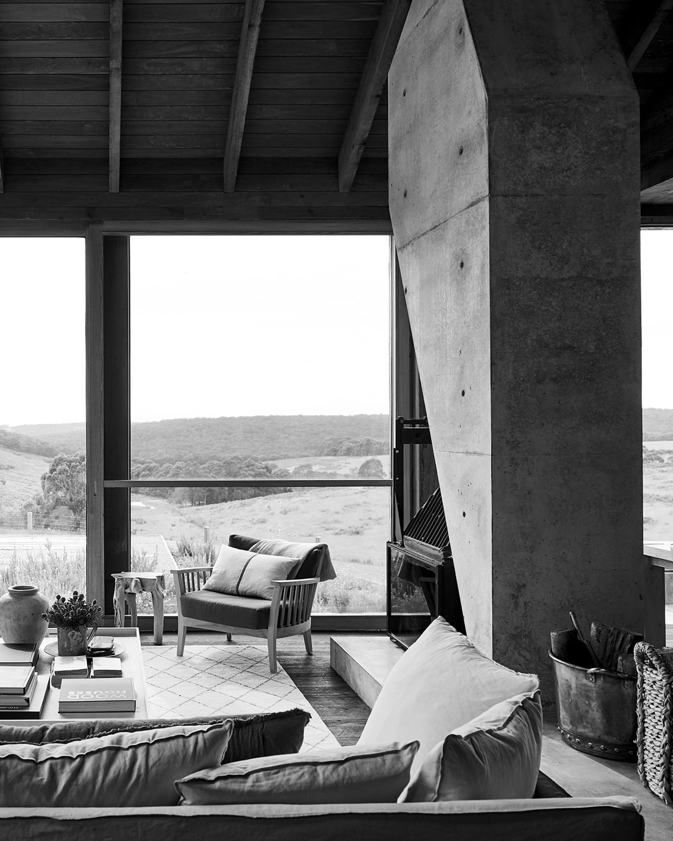 The living room of The Wensley private home, featuring a concrete floor-to-ceiling fireplace, couches and coffee table, overlooking farmland